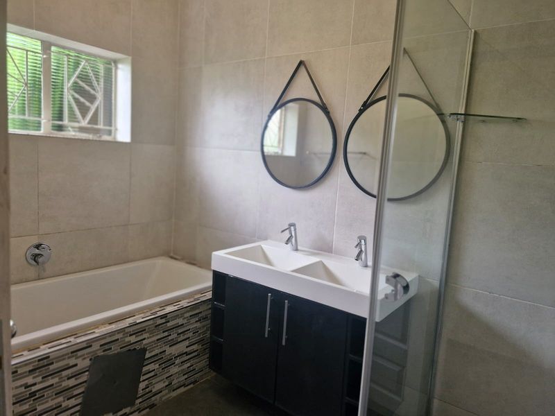 Modern bathroom featuring a double vanity, built-in bathtub, and glass shower enclosure with neutral wall tiling.