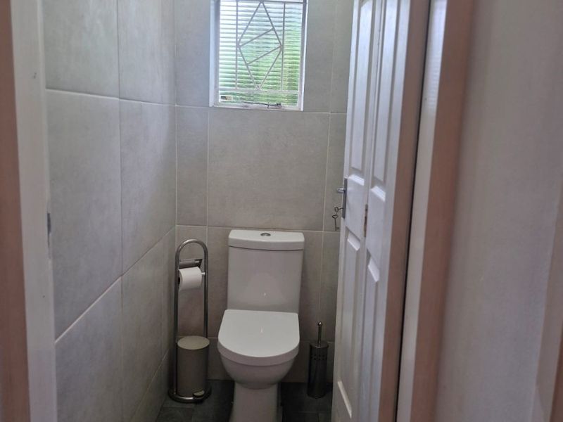 A compact, well-maintained guest bathroom featuring neutral wall tiles, dark floor tiles, and a modern toilet suite.