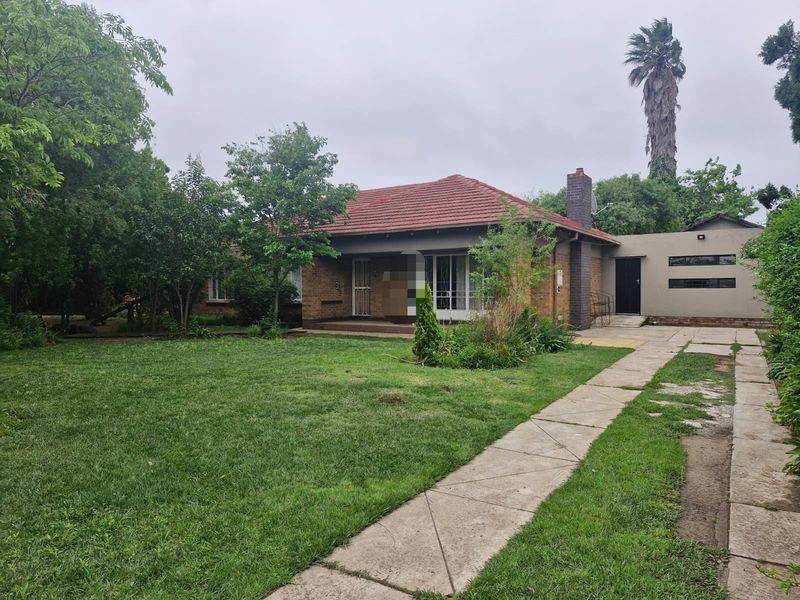Front view of a single-story brick house featuring a tiled roof, covered porch, and a spacious front garden with a concrete driveway.
