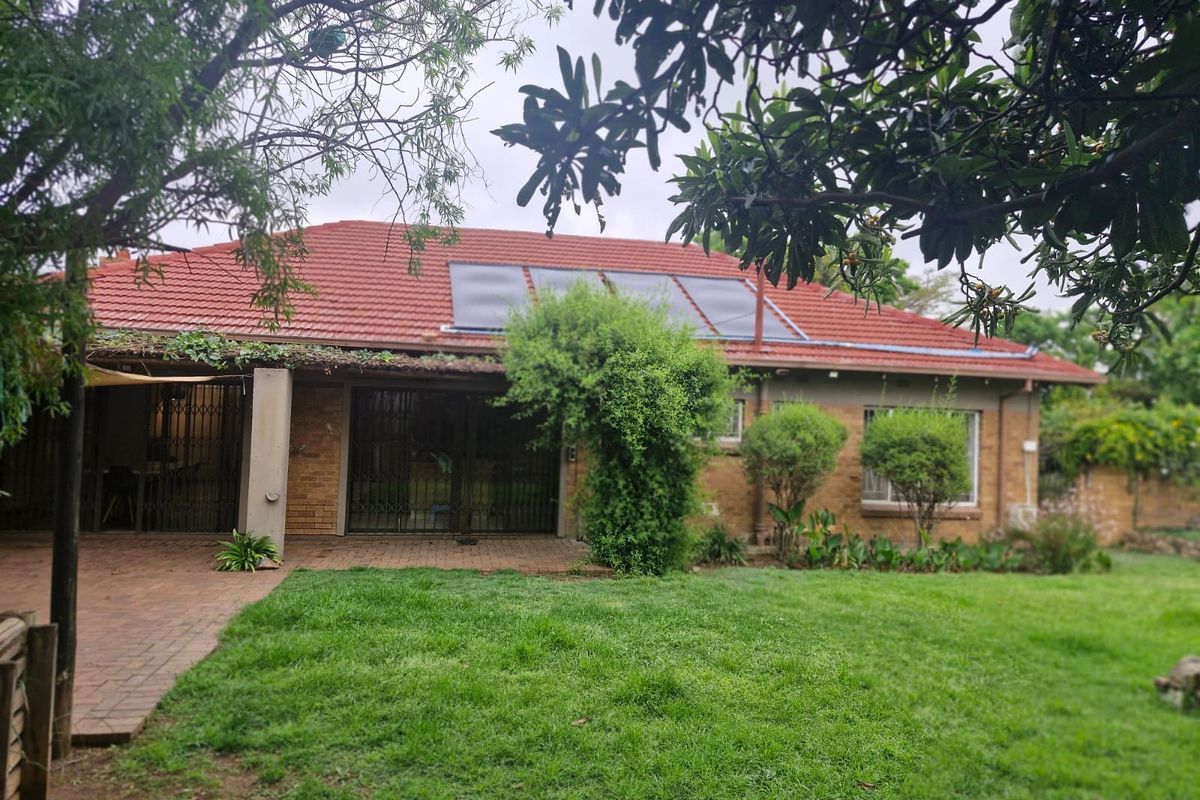Rear view of the house featuring a tiled roof with solar panels, a paved patio area, and a well-maintained garden.