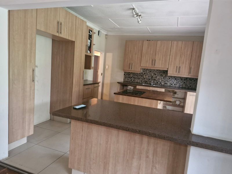 A functional kitchen featuring light wood-look cabinetry, stone countertops, and a mosaic tile backsplash, currently requiring minor repairs to cabinetry.