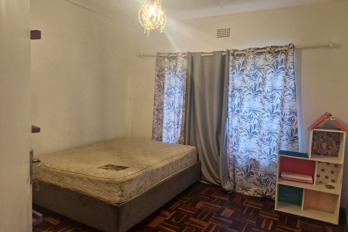 A bedroom featuring classic parquet flooring and a ceiling vent, showing signs of wear and ceiling water staining requiring maintenance.