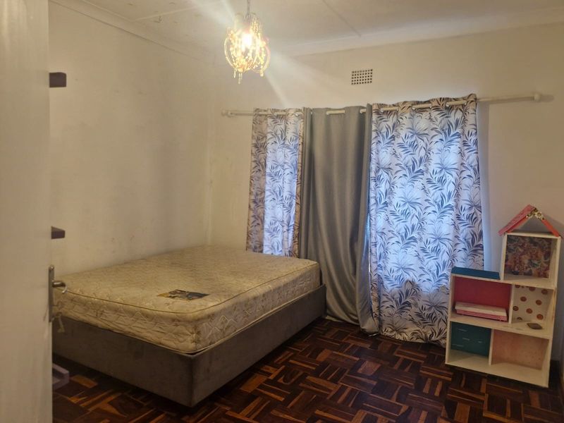 A bedroom featuring classic parquet flooring and a ceiling vent, showing signs of wear and ceiling water staining requiring maintenance.