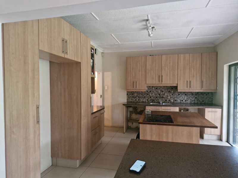 Kitchen featuring light wood-look cabinetry, a central island with a hob, mosaic tile backsplash, and tiled flooring. Requires minor repairs to cabinetry and wall finishes.