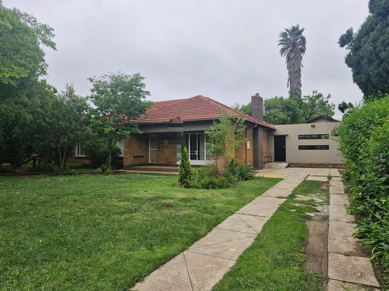 Front view of a single-story brick house featuring a tiled roof, chimney, and a concrete driveway leading to the entrance.