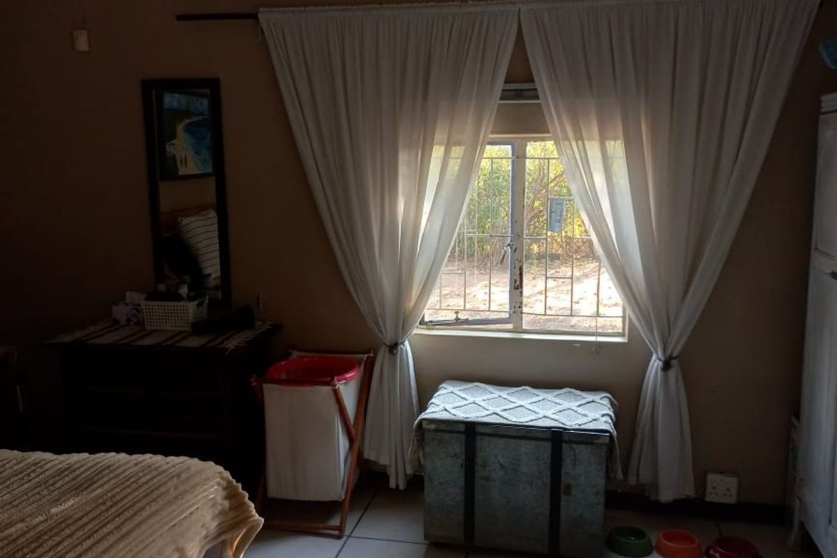 A bedroom featuring tiled flooring, a ceiling fan, and a window with security bars, requiring minor cosmetic updates to the wall finishes.
