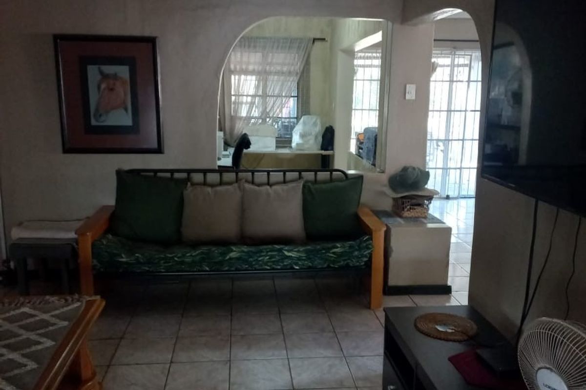 A living room featuring tiled flooring and an arched doorway leading to an adjacent space, with visible wear on the ceiling and wall finishes.