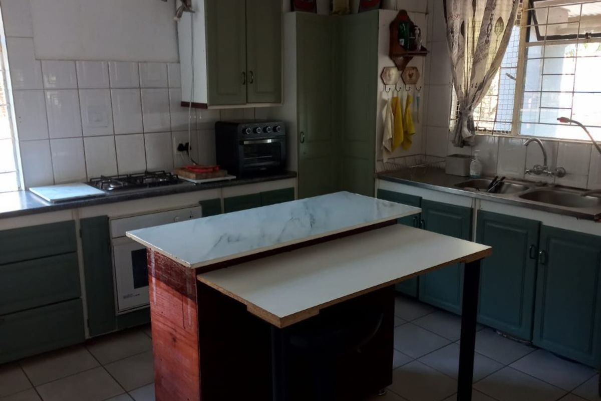 A functional kitchen featuring built-in cabinetry, a gas hob, built-in oven, double basin sink, and tiled flooring with a central prep island.