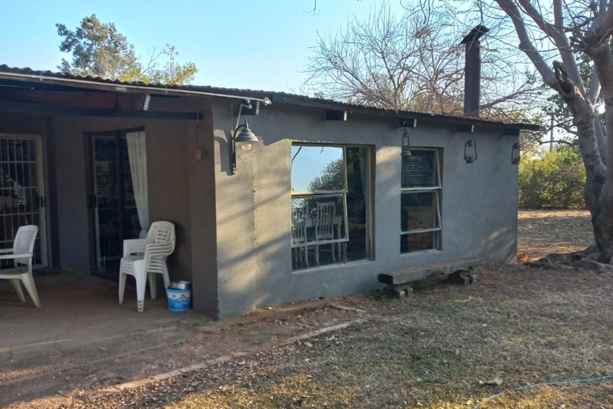 Rear view of a farm dwelling featuring a corrugated metal roof, chimney, sliding glass doors, and a concrete patio area.
