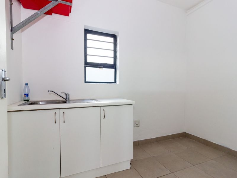 A functional laundry area featuring a stainless steel sink, base cabinetry, tiled flooring, and a window with security bars.
