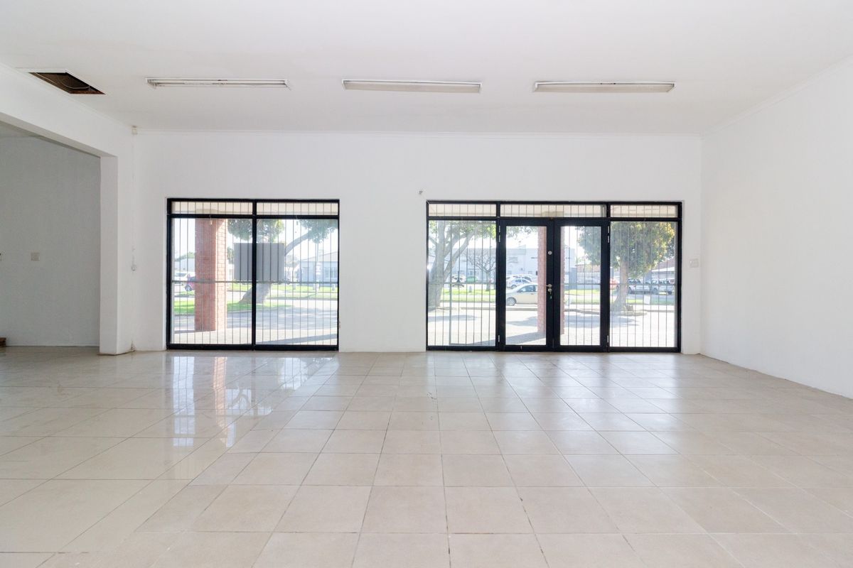 Spacious open-plan retail area featuring tiled flooring, large glass display doors with security gates, and overhead fluorescent lighting.