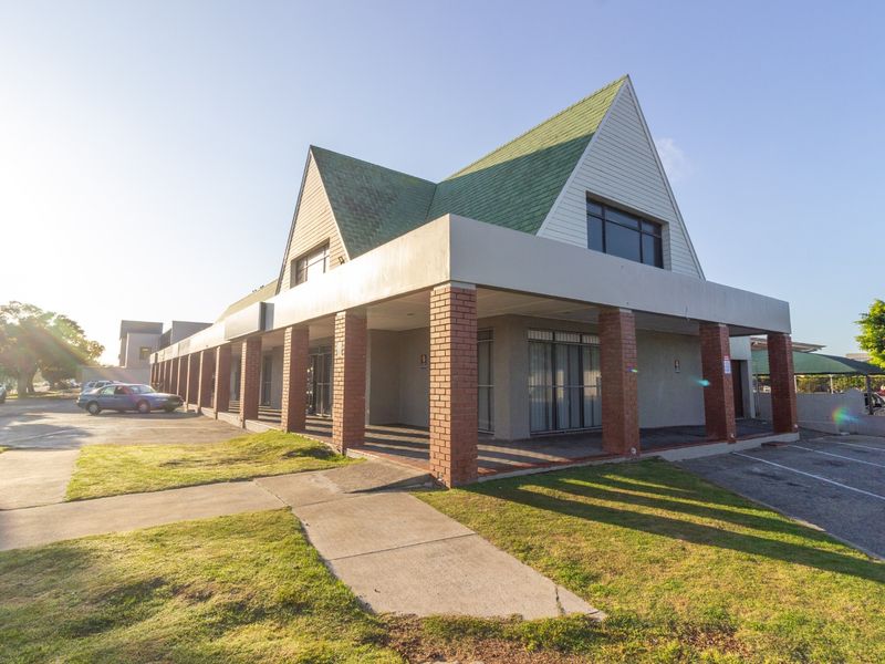 Front exterior view of a retail property featuring a covered walkway with brick columns and a distinctive pitched roof design.