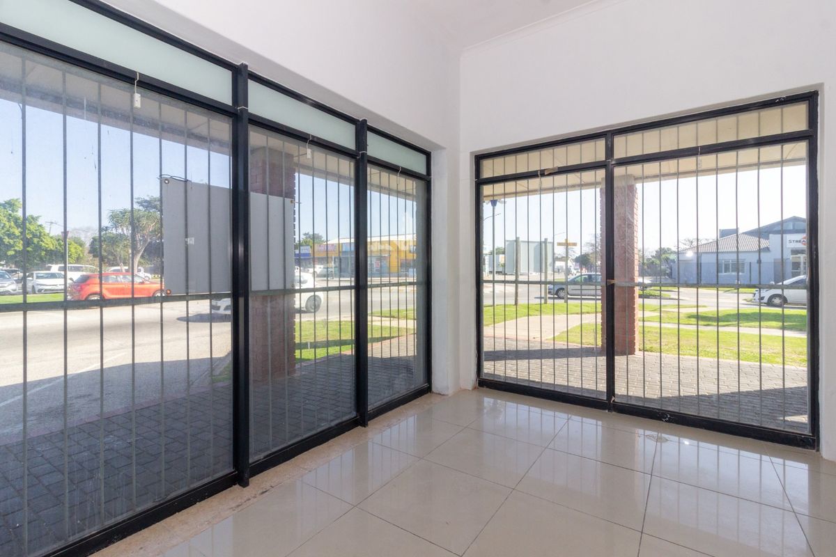 Bright and open retail entrance area featuring large glass doors with security bars, tiled flooring, and views of the street.