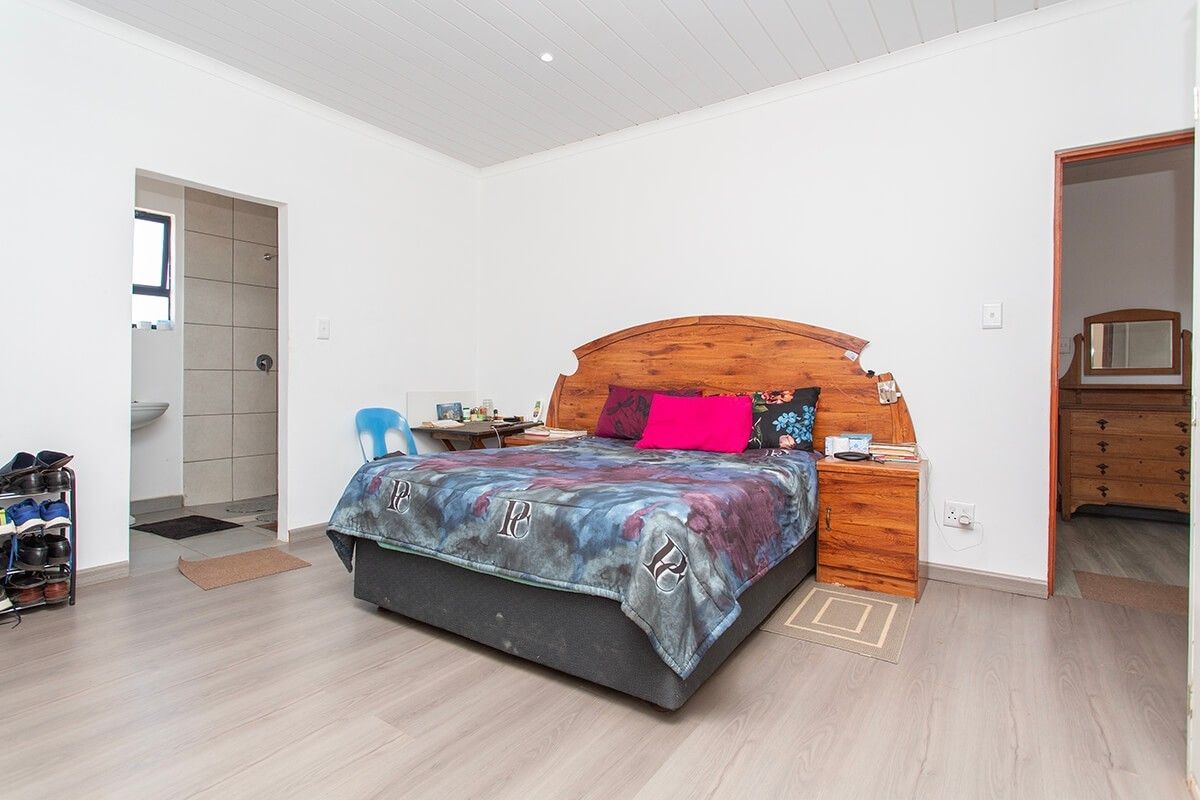 A spacious bedroom featuring light-toned laminate flooring, a white tongue and groove ceiling, and direct access to an en-suite bathroom.