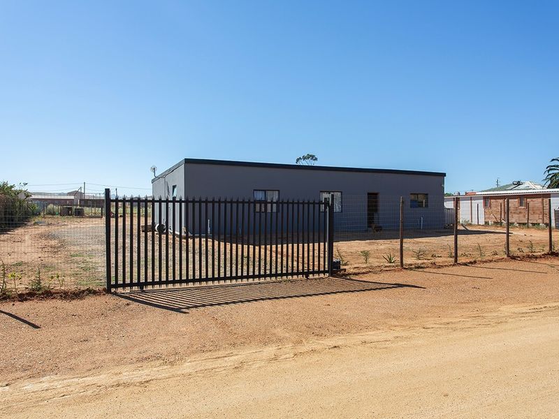 Front view of a detached property featuring a metal security gate, wire mesh fencing, and a gravel driveway on a small holding.