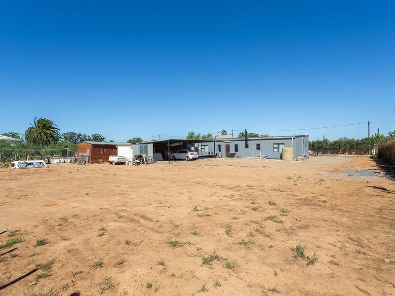 Wide view of the rear exterior of the property, featuring a large open yard, a carport, and an outbuilding on a small holding.