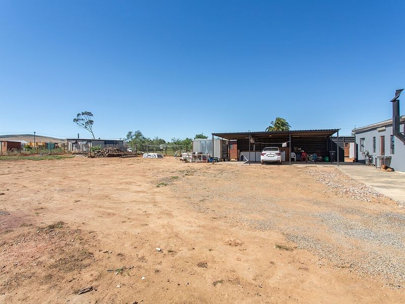 Spacious rear yard area featuring a large carport structure, concrete driveway, and open land, offering significant potential for landscaping or further development.