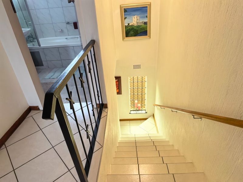 A bright staircase featuring tiled steps, a metal balustrade with a wooden handrail, and a decorative leaded glass window.