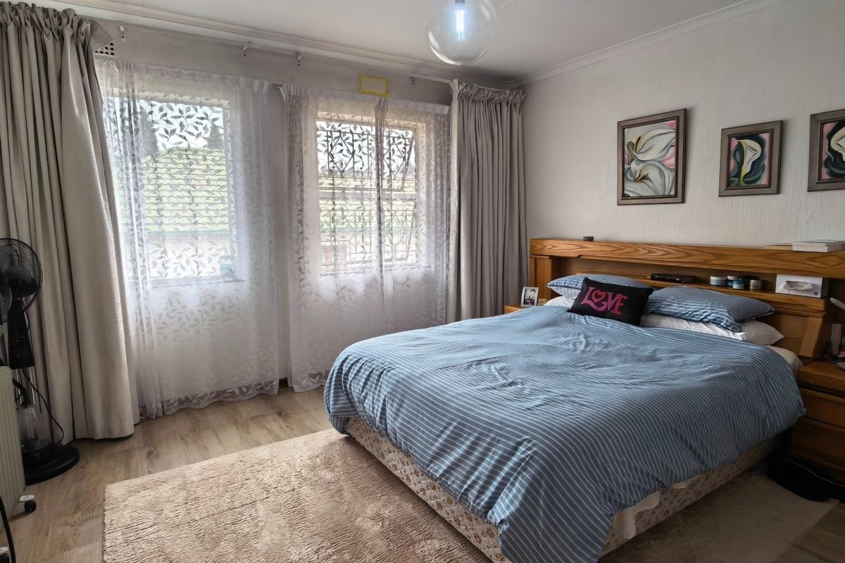 A well-maintained bedroom featuring laminate flooring, a built-in wooden headboard, and large windows with natural light.