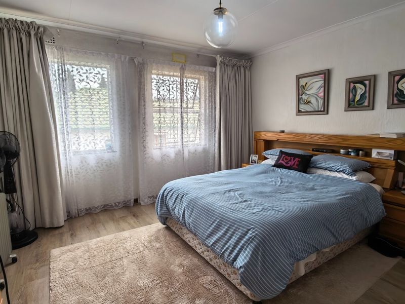 A well-maintained bedroom featuring laminate flooring, a built-in wooden headboard, and large windows with natural light.