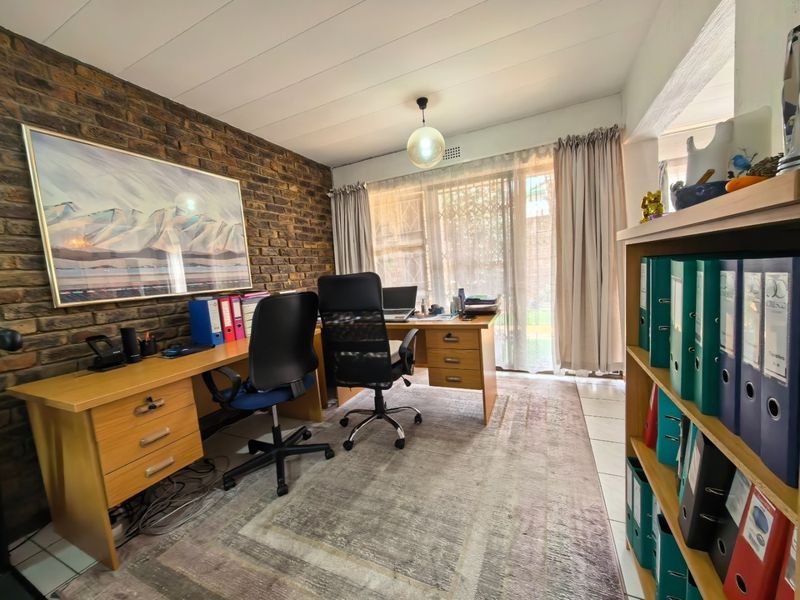 A functional home office featuring an exposed brick wall, tiled flooring, and large windows providing natural light.