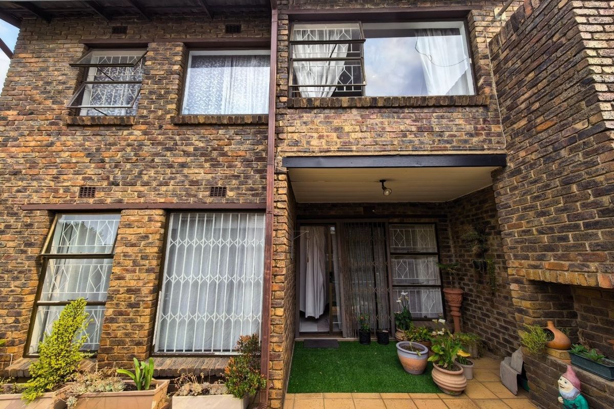 Rear exterior view of a face brick apartment featuring a covered patio area, security gates, and a built-in brick fireplace.