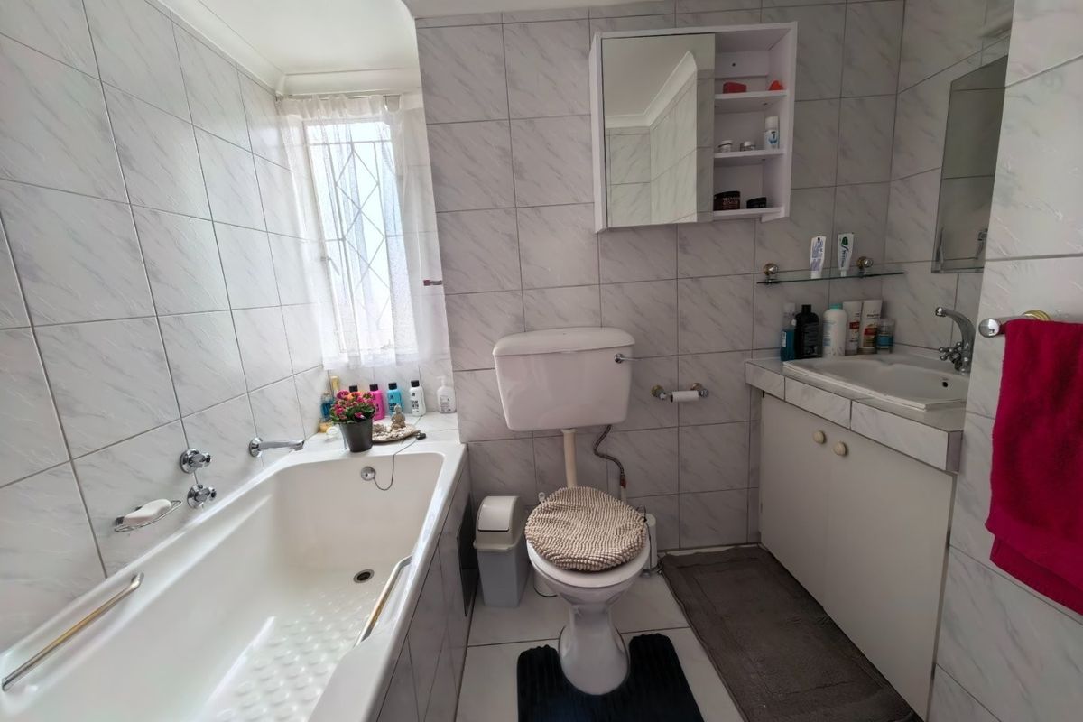 A functional bathroom featuring a bathtub, toilet, and vanity cabinet with integrated basin, finished with neutral wall and floor tiles.