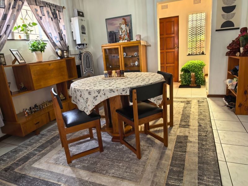 A dining area featuring tiled flooring, a wall-mounted gas geyser, and access to an adjacent hallway with security features.