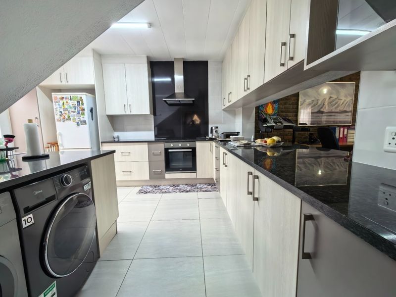 Modern kitchen featuring light wood-finish cabinetry, dark granite countertops, built-in oven with extractor fan, and tiled flooring with an integrated washing machine.