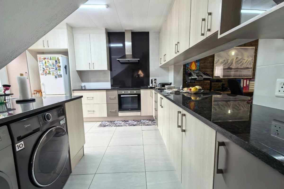 Modern kitchen featuring light wood-finish cabinetry, dark granite countertops, built-in oven with extractor fan, and tiled flooring with an integrated washing machine.