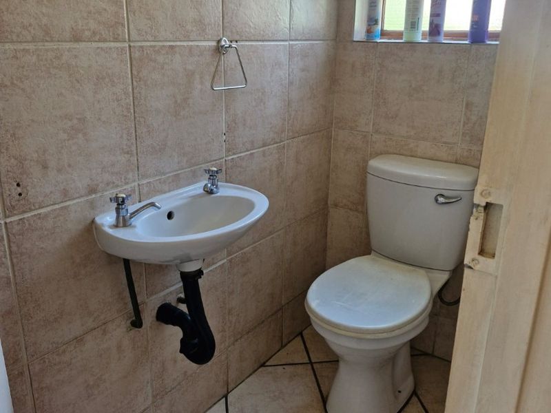 A compact guest bathroom featuring a wall-mounted basin, standard toilet, and neutral ceramic tiling throughout.