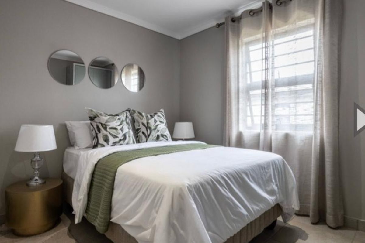 A well-maintained bedroom featuring neutral grey walls, tiled flooring, and a window fitted with security bars.