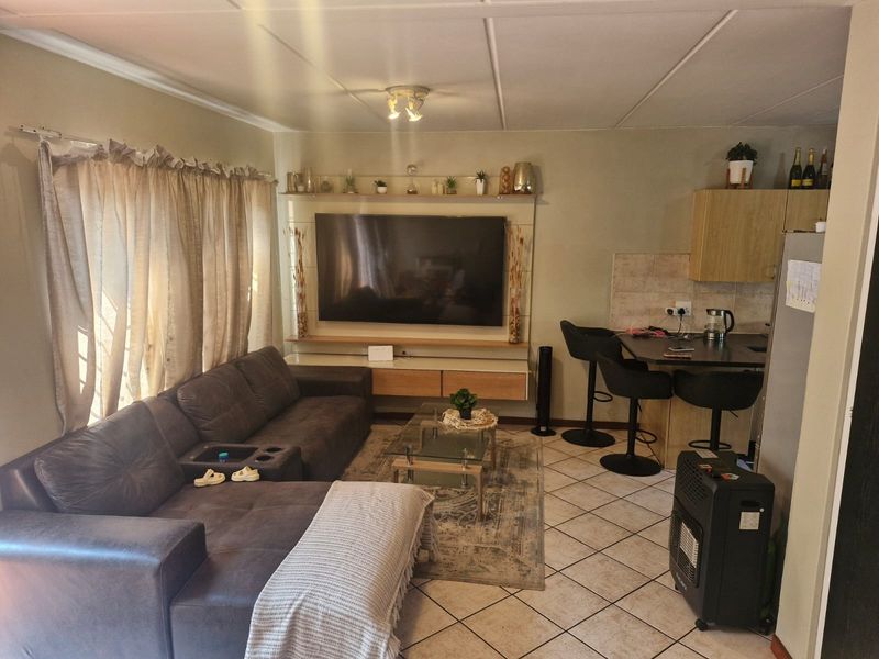 Open-plan living area featuring a built-in media wall, tiled flooring, and a compact kitchen with a breakfast bar.