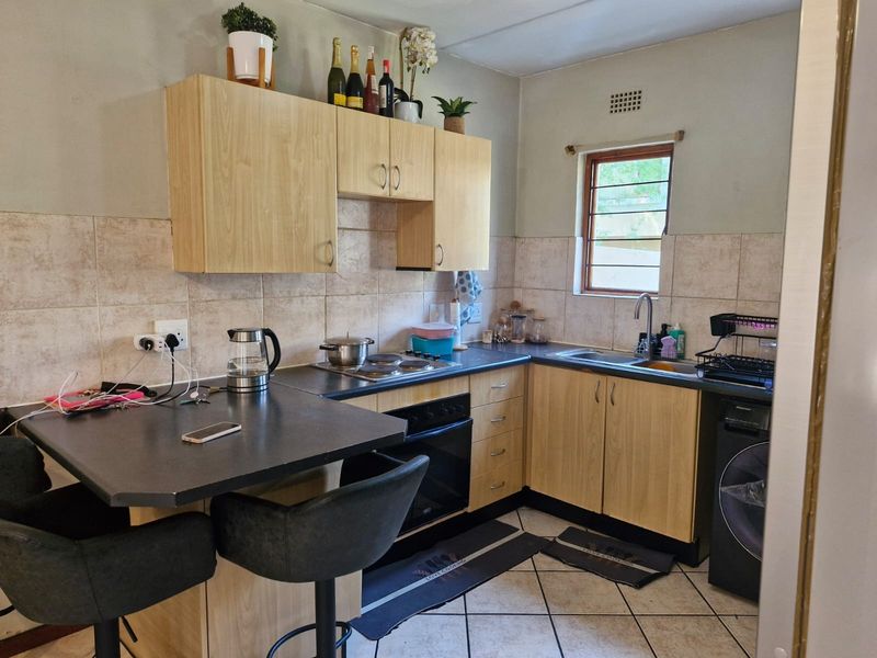 A functional kitchen featuring light wood cabinetry, dark laminate countertops, a breakfast bar, built-in oven and hob, and tiled flooring.