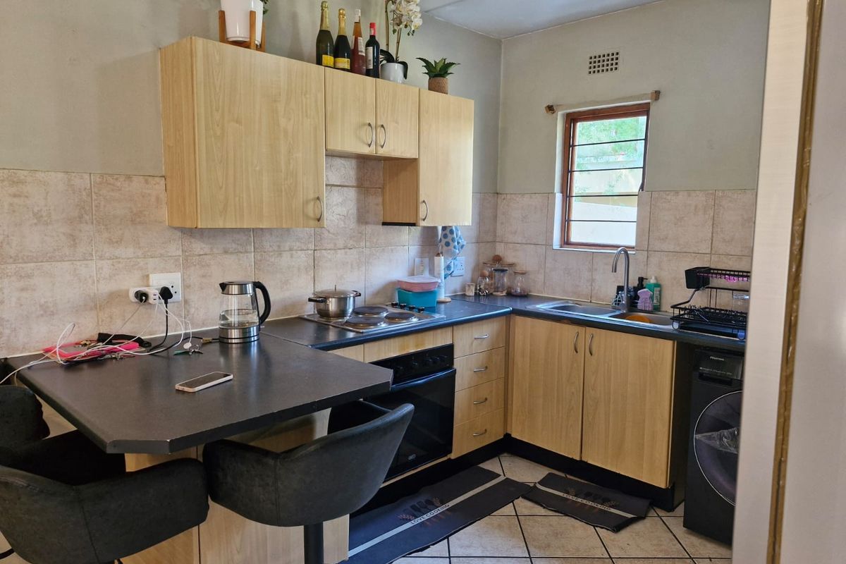 A functional kitchen featuring light wood cabinetry, dark laminate countertops, a breakfast bar, built-in oven and hob, and tiled flooring.