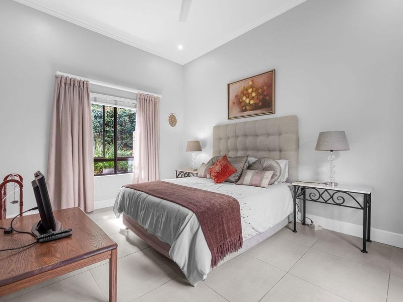 A well-maintained bedroom featuring neutral tiled flooring, a ceiling fan, and natural light from a window.