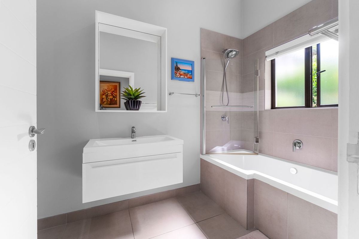 Modern bathroom featuring a wall-mounted vanity with integrated basin, mirror cabinet, and a shower-over-bath combination with tiled finishes.