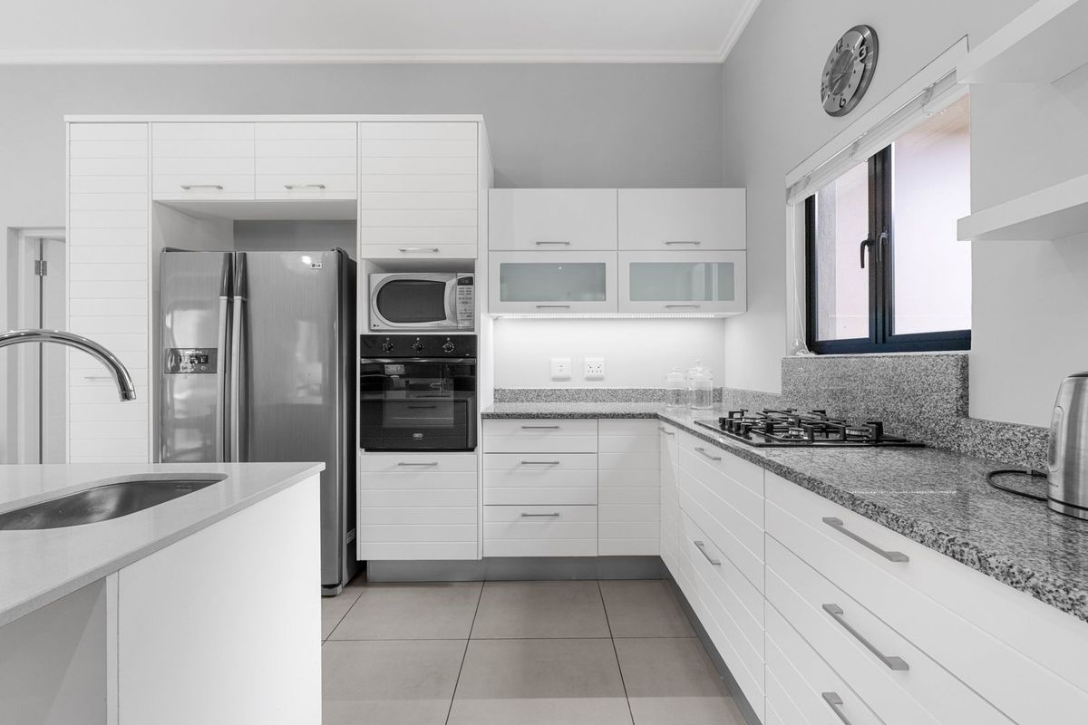 Modern kitchen featuring white cabinetry, granite countertops, a gas hob, built-in oven, microwave, and a functional island with a sink.