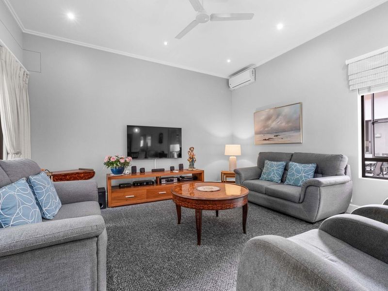 A well-maintained living room featuring neutral walls, carpeted flooring, a ceiling fan, and a split-system air conditioner for climate control.