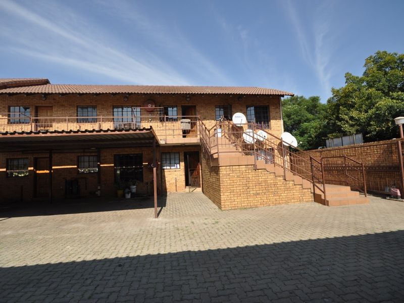 Exterior view of a face brick apartment complex featuring a paved driveway, covered carport, and an external staircase leading to upper-level units.