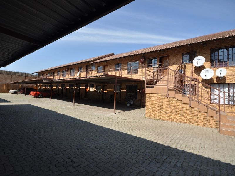 Exterior view of a multi-story apartment complex featuring face-brick construction, a paved parking area with covered carports, and external staircases.