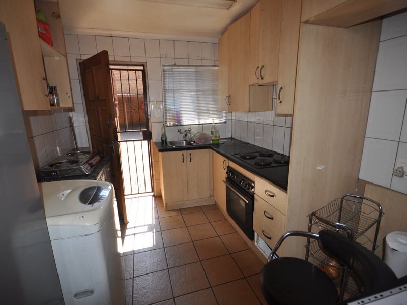 Compact kitchen featuring built-in cabinetry, electric hob, oven, and tiled finishes, with direct access to an exterior area via a security gate.