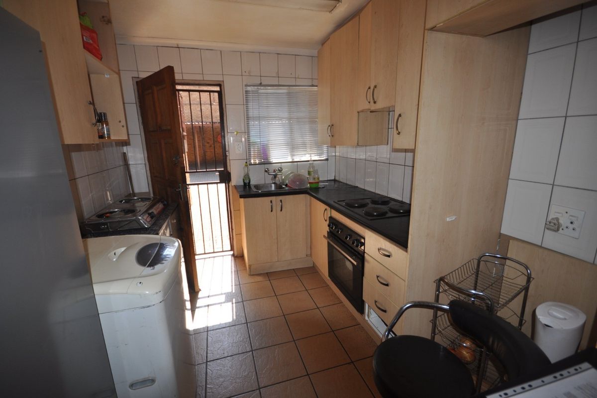 Compact kitchen featuring built-in cabinetry, electric hob, oven, and tiled finishes, with direct access to an exterior area via a security gate.