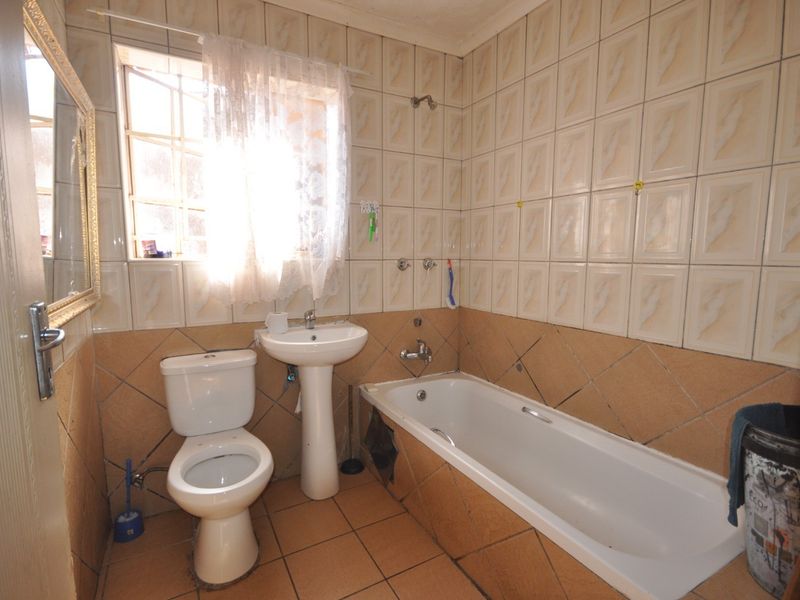 A dated bathroom featuring a standard bathtub, pedestal basin, and toilet with full-height wall tiling and floor tiles.