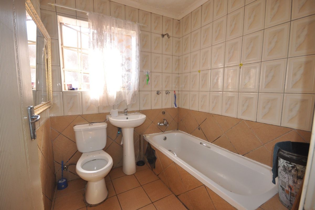 A dated bathroom featuring a standard bathtub, pedestal basin, and toilet with full-height wall tiling and floor tiles.