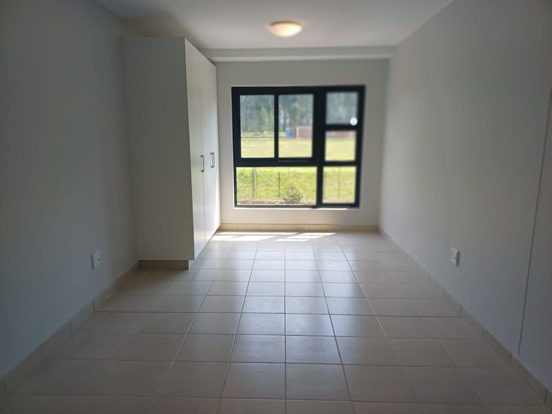 A clean, empty bedroom featuring neutral tiled flooring, a built-in wardrobe, and a large window providing natural light.