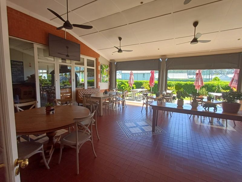 Spacious covered patio area featuring tiled flooring, exposed brick accents, ceiling fans, and retractable blinds, providing a versatile outdoor dining or entertainment space.