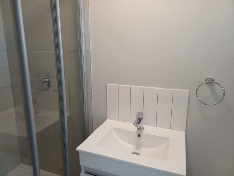 A clean, modern bathroom featuring a vanity basin with a mixer tap, tiled splashback, and a glass-enclosed shower.