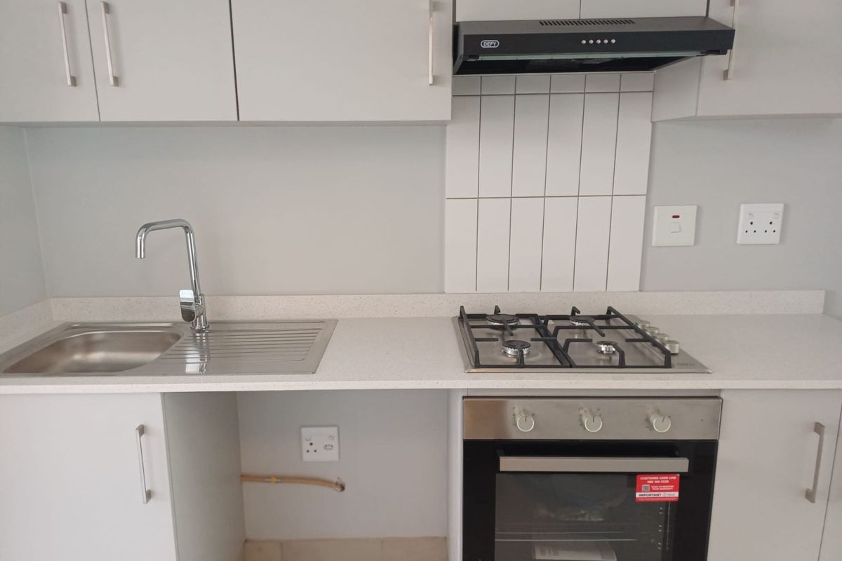 A modern, clean kitchen featuring light grey cabinetry, stone countertops, a gas hob, built-in oven, and a stainless steel sink with a tiled splashback.