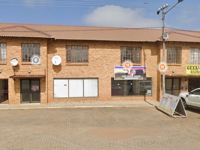 Front elevation of a multi-unit brick retail complex featuring tiled roofing, aluminium window frames, and an open paved parking area.